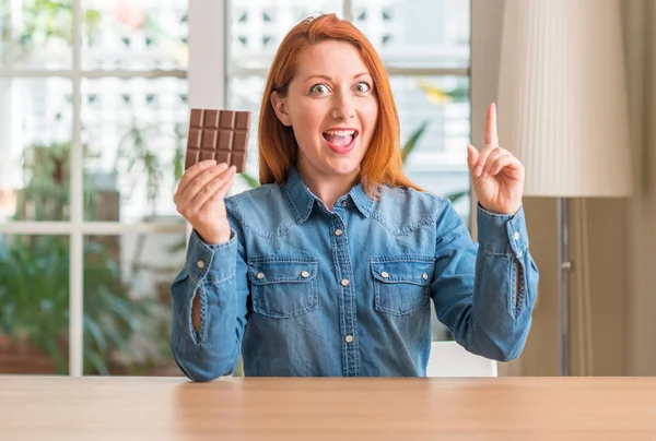 Mulher Ruiva Segurando Barra Chocolate Casa Surpreso Com Uma Ideia — Fotografia de Stock