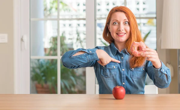 赤毛の女性を自分に指を指して驚き顔でアップルとドーナツの選択します — ストック写真