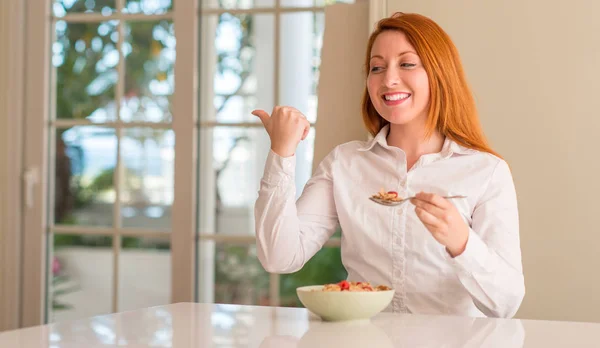 红头发的女人吃谷物与树莓在家里指着手和手指与快乐的脸微笑 — 图库照片