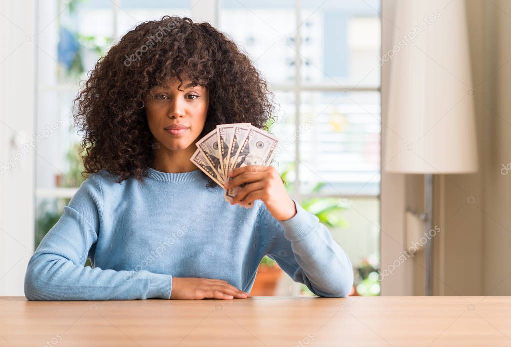 African american woman holding dollar bank notes with a confident expression on smart face thinking serious