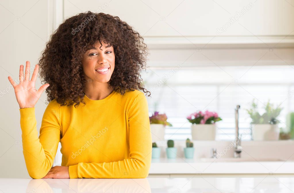 African american woman wearing yellow sweater at kitchen showing and pointing up with fingers number five while smiling confident and happy.