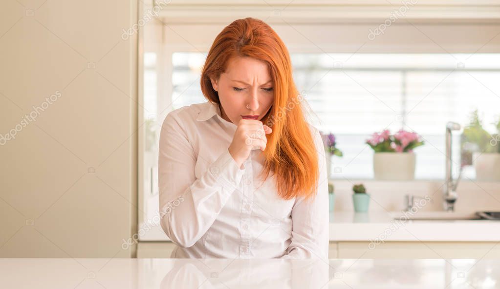 Redhead woman at kitchen feeling unwell and coughing as symptom for cold or bronchitis. Healthcare concept.