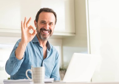Dizüstü evde kullanan orta yaş adam parmak, mükemmel sembolü ile ok işareti yapıyor