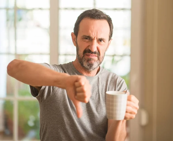 中年男性の怒った顔 ダウン親指で嫌悪感を示すマイナス記号 拒絶反応の概念でカップでコーヒーを飲む — ストック写真