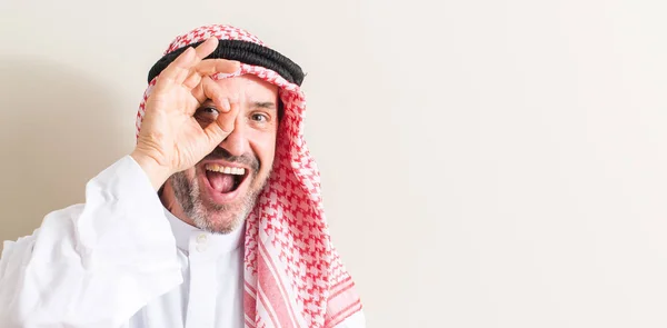 指を通して見る目に手で サインをして笑っている幸せそうな顔を持つ上級アラビア語男 — ストック写真