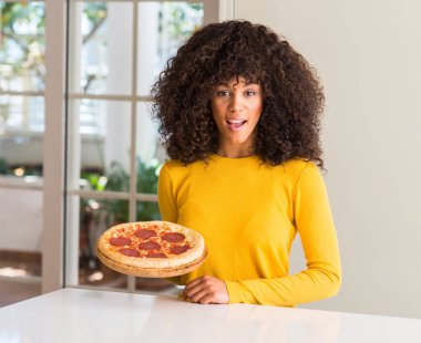 Afrikalı-Amerikalı kadın evde lezzetli biberli pizza yemeye hazır korkuyor şok sürpriz yüz, korkuyor ve heyecanlı korku ifadesi ile