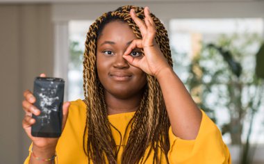 Afrikalı-Amerikalı kadın mutlu yüz el parmaklarının arasından seyir göz üzerinde ok işaretiyle yapıyor gülümseyen ile kırık smartphone gösterilen