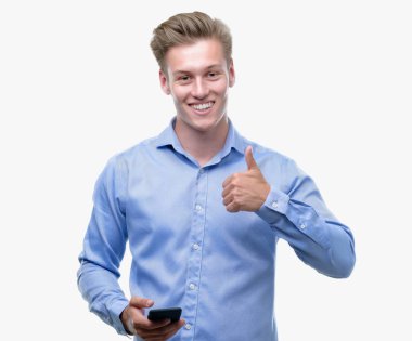 Ok işareti, başparmak ile parmak, mükemmel işareti yapıyor kocaman bir gülümseme ile Smartphone mutlu kullanan genç yakışıklı sarışın adam