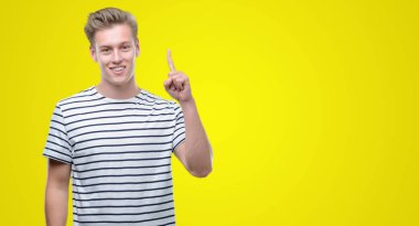 Genç yakışıklı sarışın adam giyen çizgili denizci bir fikir ya da soru işaret parmağı gülen yüz, bir numara ile t-shirt şaşırttı