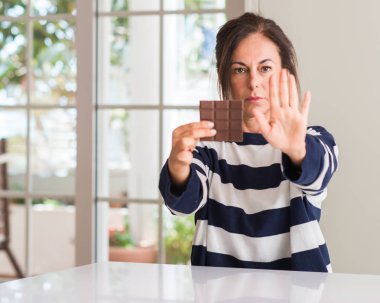 Orta yaşlı kadın açık eliyle dur işareti ile ciddi ve kendine güvenen ifade, savunma jest yapıyor çikolata yeme