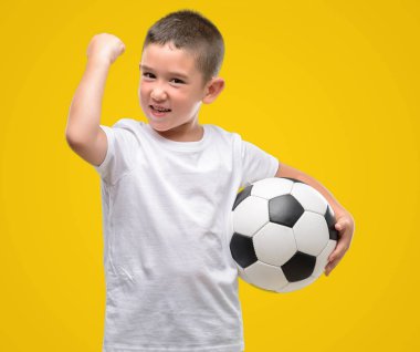 Koyu saçlı küçük çocuk futbol oynamak top ile öfke, çılgın ve yükseltilmiş eliyle diye bağıran rahatsız ve hayal kırıklığına uğramış öfke kavramı bağırarak