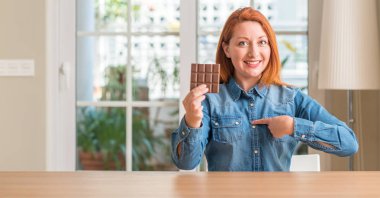 Evde kendisi için sürpriz yüz işaret parmağı ile çikolata bar tutan Kızıl saçlı kadın