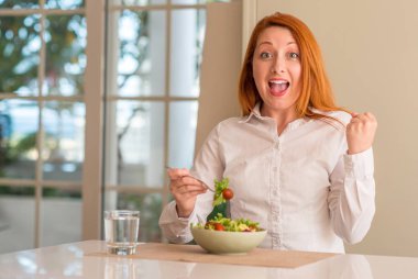 Duygu tezahürat ev gurur çığlık ve kutluyor zafer ve çok heyecanlı, başarı, taze yeşil salata yemek Kızıl saçlı kadın