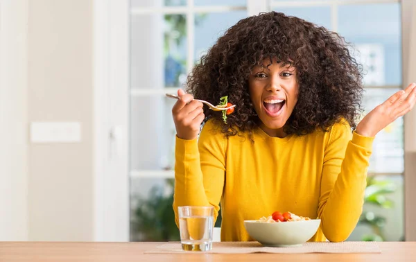 非洲裔美国妇女在家里吃面食沙拉非常高兴和兴奋 优胜者表达庆祝胜利尖叫着大微笑和举手 — 图库照片