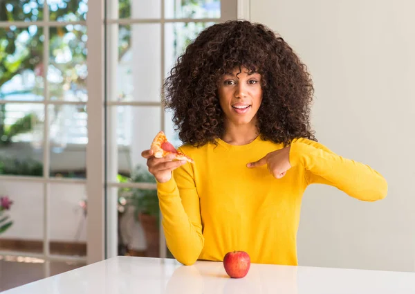 非洲裔美国妇女选择苹果和比萨饼切片与惊讶的脸指向自己的手指 — 图库照片