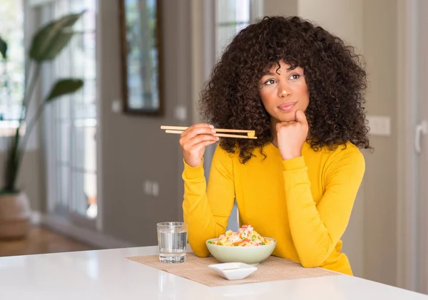African american woman eating asian rice at home serious face thinking about question, very confused idea