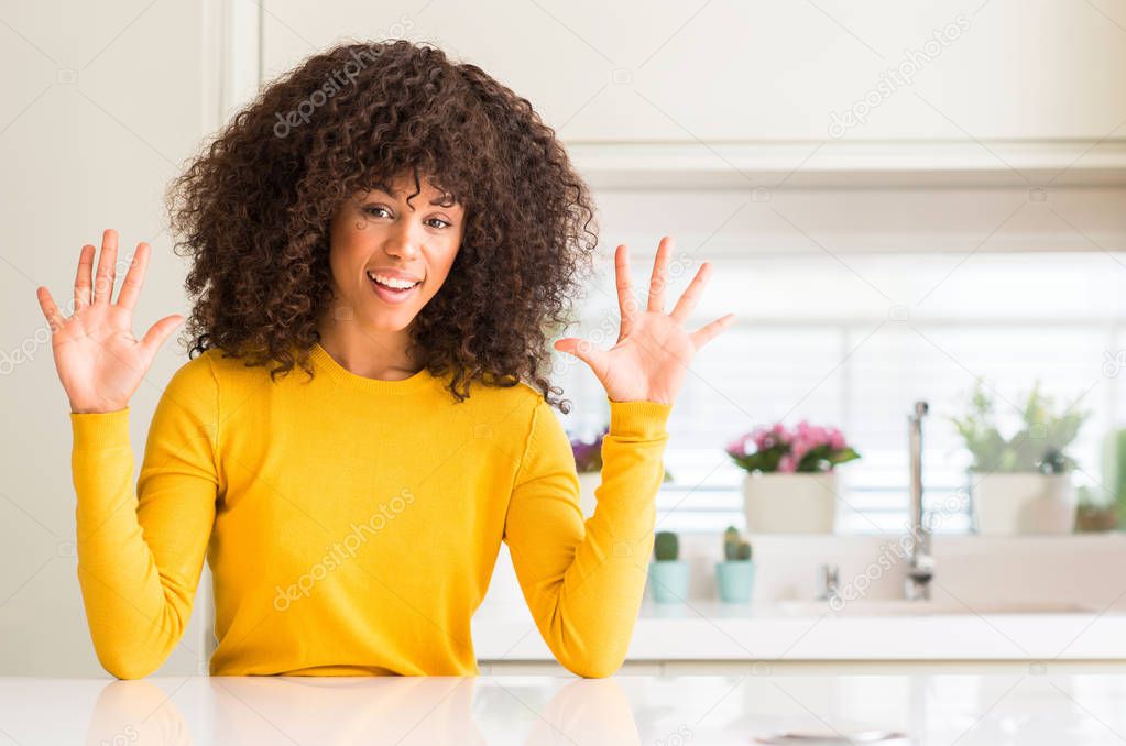 African american woman wearing yellow sweater at kitchen showing and pointing up with fingers number ten while smiling confident and happy.