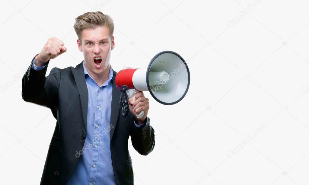 Young handsome blond man holding a megaphone annoyed and frustrated shouting with anger, crazy and yelling with raised hand, anger concept