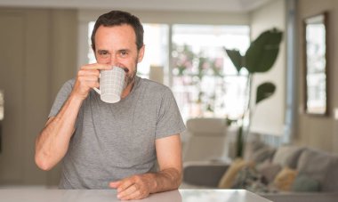 Orta yaş adam ayakta ve diş gösterilen kendine güvenen bir gülümsemeyle gülümseyerek mutlu bir yüz ile bir fincan kahve içme