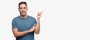 Yüzünde kocaman bir gülümseme ile yakışıklı genç casual adam kameraya bakarak yan el ve parmak ile işaret.
