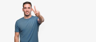 Zafer işareti yapıyor parmak gösterilen kamera seyir gülümseyen yakışıklı genç casual adam. İki numaralı.