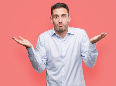 Yakışıklı genç işadamı clueless ve şaşkın bir ifadeyle kollar ve eller kaldırdı. Şüphe kavramı.