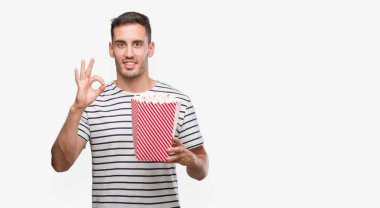 Yakışıklı genç adam yeme patlamış mısır parmak, mükemmel sembolü ile ok işareti yapıyor