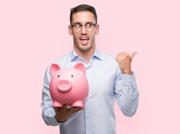 Handsome Young Man Holding Piggy Bank Pointing Hand Finger Happy — Stock Photo, Image