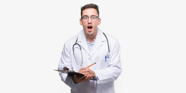 Handsome Young Doctor Man Holding Clipboard Scared Shock Surprise Face — Stock Photo, Image
