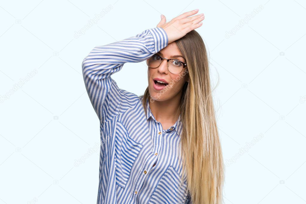 Beautiful young woman wearing elegant shirt and glasses surprised with hand on head for mistake, remember error. Forgot, bad memory concept.