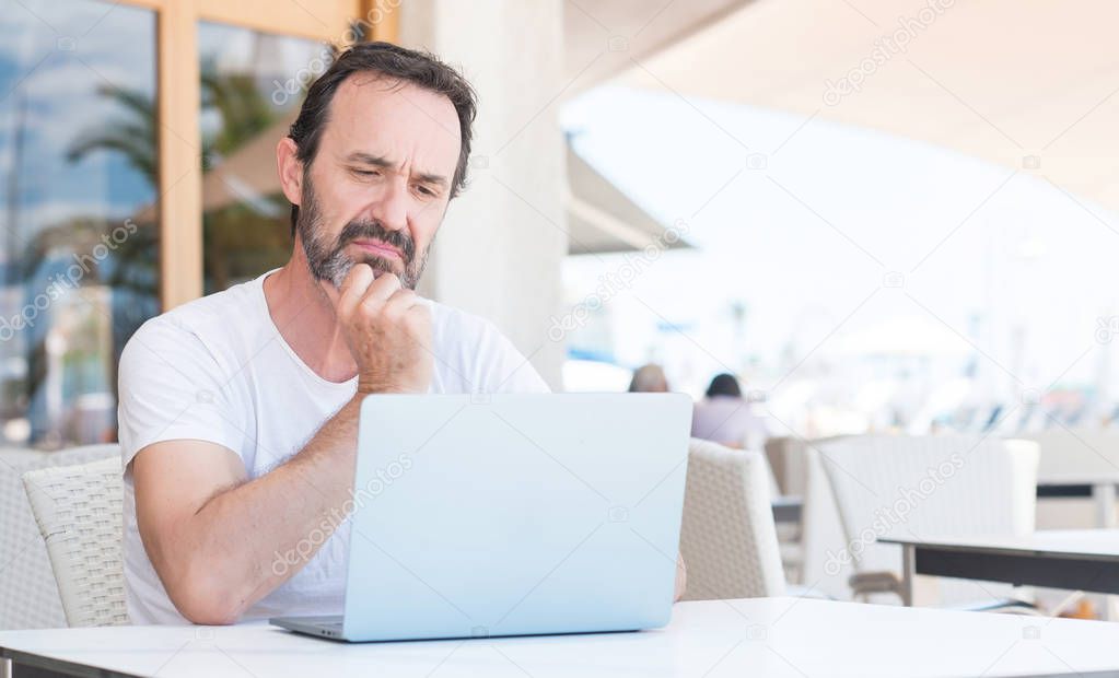 Handsome senior man using laptop at restaurant serious face thinking about question, very confused idea