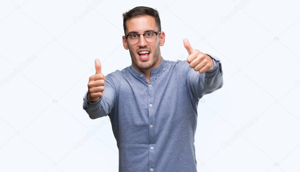Handsome young elegant man wearing glasses approving doing positive gesture with hand, thumbs up smiling and happy for success. Looking at the camera, winner gesture.