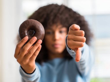 Young african american woman holding chocolate donut at home with angry face, negative sign showing dislike with thumbs down, rejection concept clipart