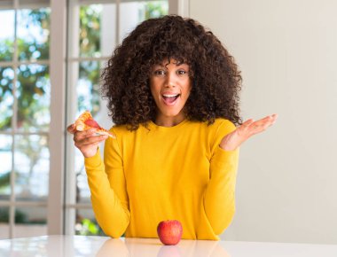 Afrikalı-Amerikalı kadın elma ve pizza arasında seçim yapma çok mutlu ve heyecanlı, kazanan ifade büyük gülümseme ile çığlık zaferini kutluyor dilim ve ellerini kaldırdı