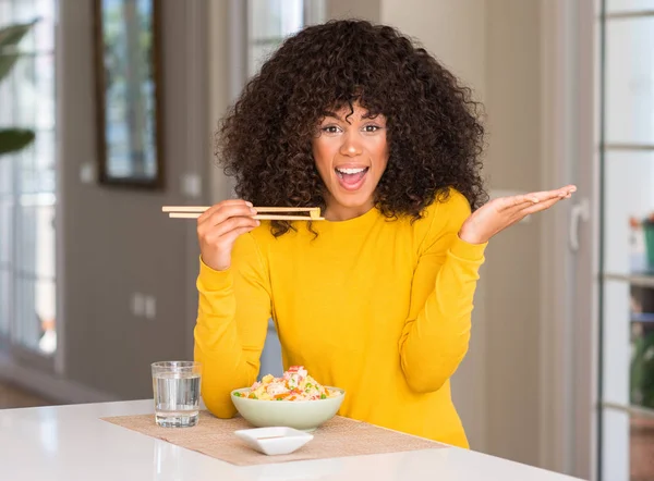 African american woman eating asian rice at home very happy and excited, winner expression celebrating victory screaming with big smile and raised hands