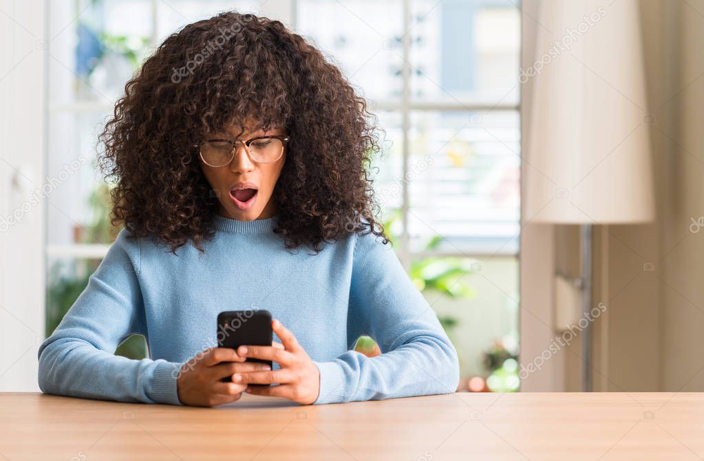 Beautiful african american woman using smartphone scared in shock with a surprise face, afraid and excited with fear expression