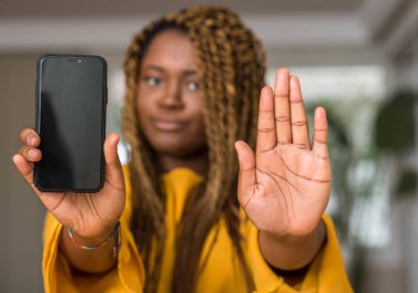 Afrikalı-Amerikalı kadın açık eliyle dur işareti ile ciddi ve kendine güvenen ifade, savunma jest yapıyor Smartphone kullanarak
