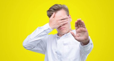 Genç yakışıklı sarışın adam ellerini gözlerinle kapsayan ve stop jest ile acı ve korku ifadesi. Utandım ve negatif kavramı.