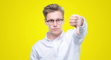 Young handsome blond man looking unhappy and angry showing rejection and negative with thumbs down gesture. Bad expression. clipart