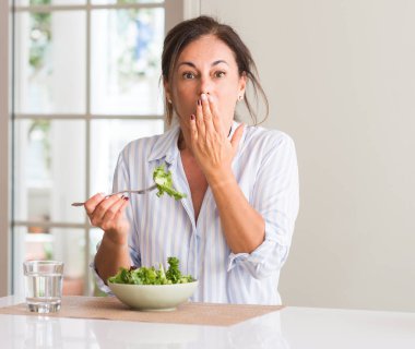 Orta yaşlı kadın evde hata, korku, ifade için utanç ile kapak ağız el ile şok bir kase taze salata yemek sessizlik içinde gizli kavramı korkuttu