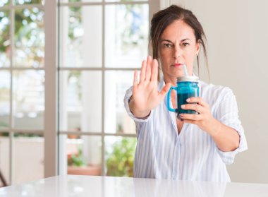 Orta yaşlı kadın açık eliyle dur işareti ile ciddi ve kendine güvenen ifade, savunma jest yapıyor bir bardak muzlu süt içme