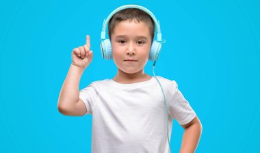 Bir fikir ya da soru işaret parmağı ile gülen yüz, bir numara koyu saçlı küçük çocuk kulaklık ile müzik dinleme şaşırttı