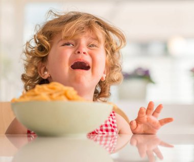 Güzel sarışın çocuk öfke nöbeti ile evde ağlıyor elleriyle spagetti yemek.