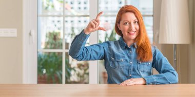 Kızıl saçlı kadın evde gülümseyen ve kendine güvenen boyutu işaret parmaklı ararken ve kamera işi el ile el hareketi. Ölçü kavramı.