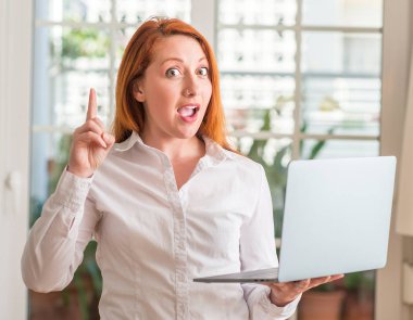 Kızıl saçlı kadın evde bilgisayar dizüstü kullanarak bir fikir ya da soru işaret parmağı ile mutlu yüz şaşırttı, number one