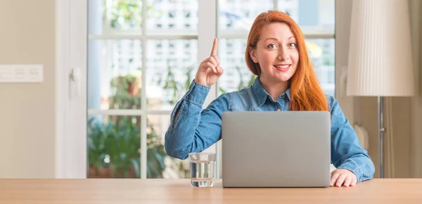 红头发的女人在家里使用电脑笔记本电脑惊讶于一个想法或问题指着一个快乐的脸 — 图库照片
