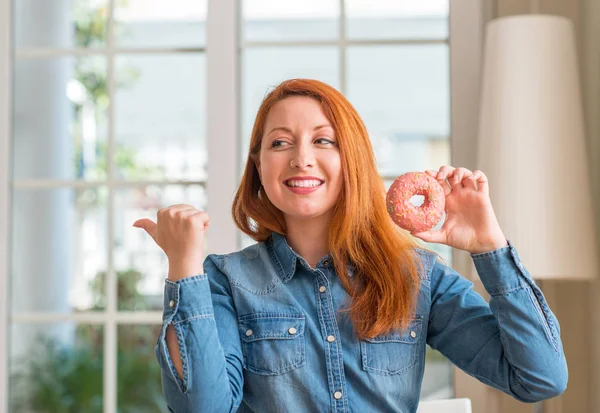 Pelirroja Sosteniendo Donut Casa Señalando Con Mano Dedo Hacia Arriba —  Fotos de Stock