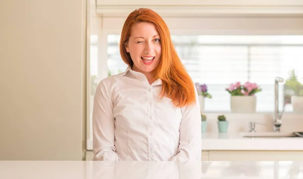 Redhead woman at kitchen winking looking at the camera with sexy expression, cheerful and happy face. — Stock Image Redhead Woman Kitchen Winking Looking Camera Sexy Expression Cheerful Happy Stock Image