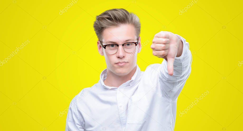 Young handsome blond man looking unhappy and angry showing rejection and negative with thumbs down gesture. Bad expression.