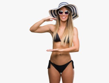 Bikini, güneş gözlüğü ve şapka ile büyük ve büyük boy işaret, ölçü birimi sembol gösteren el eller giyen güzel genç kadın. Kameraya bakarak gülümsüyordu. Ölçüm kavramı.